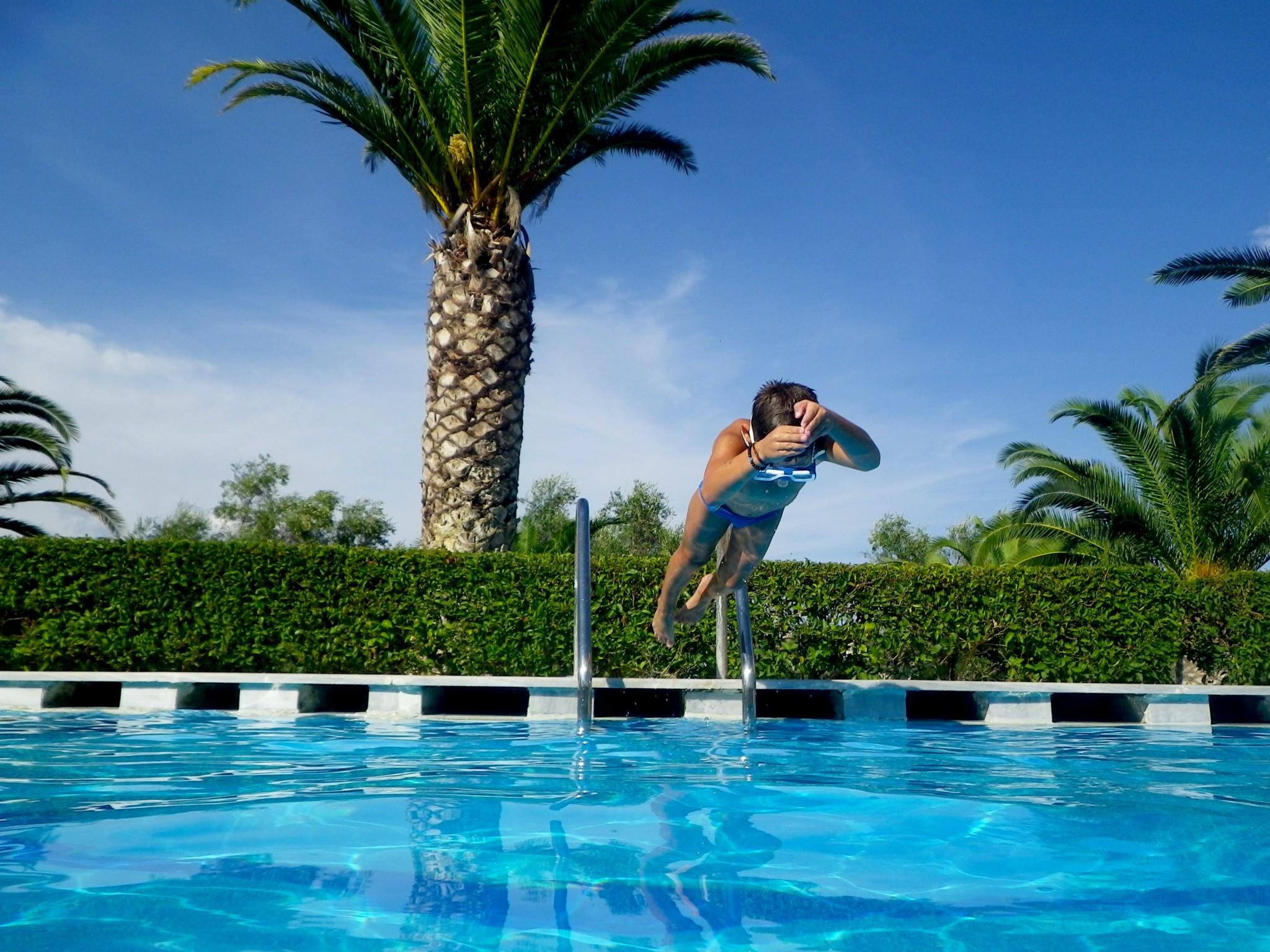 topless boy about to jump on blue swimming pool under white and blue sky during daytime