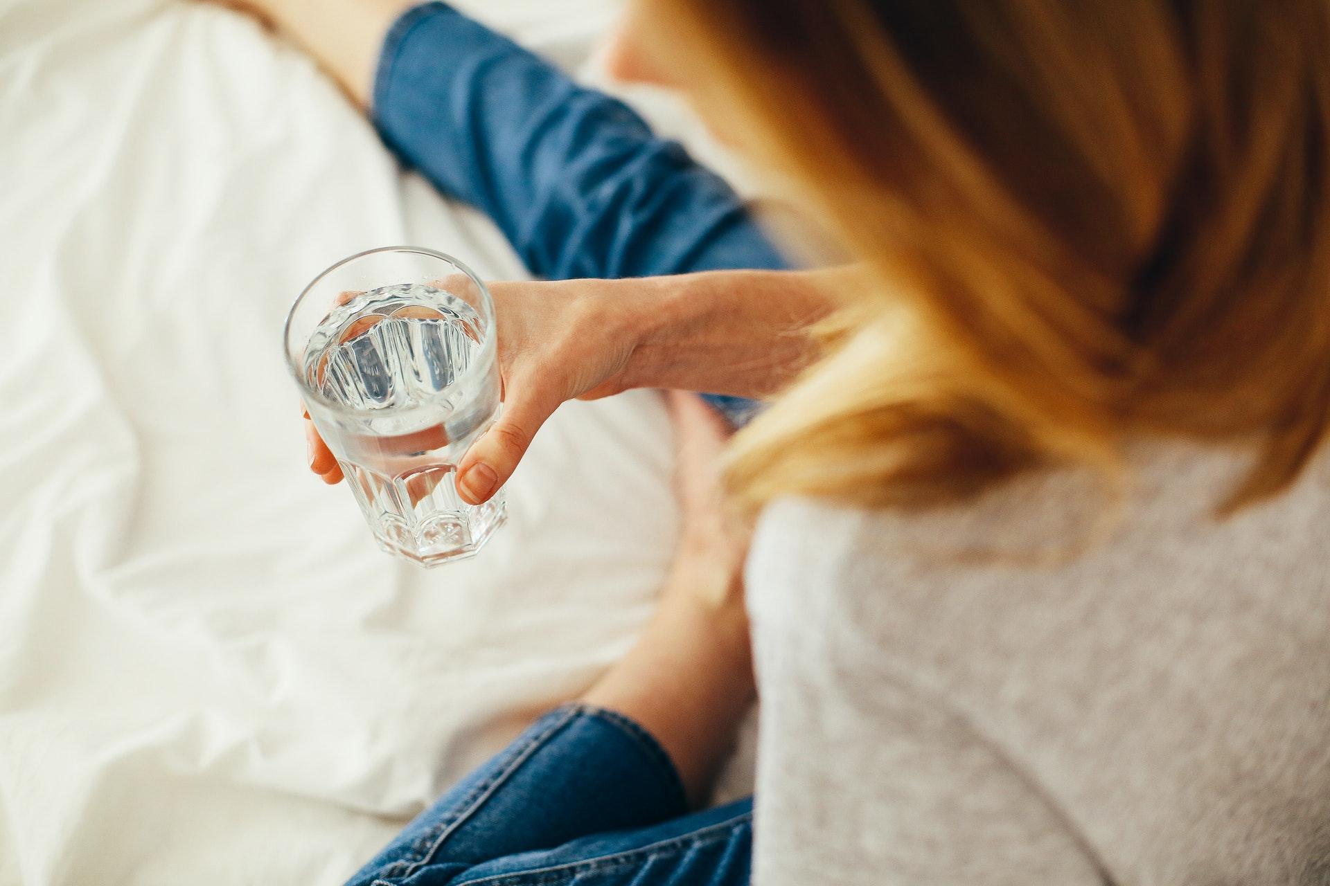 woman holding glass of water in hand laying on bed